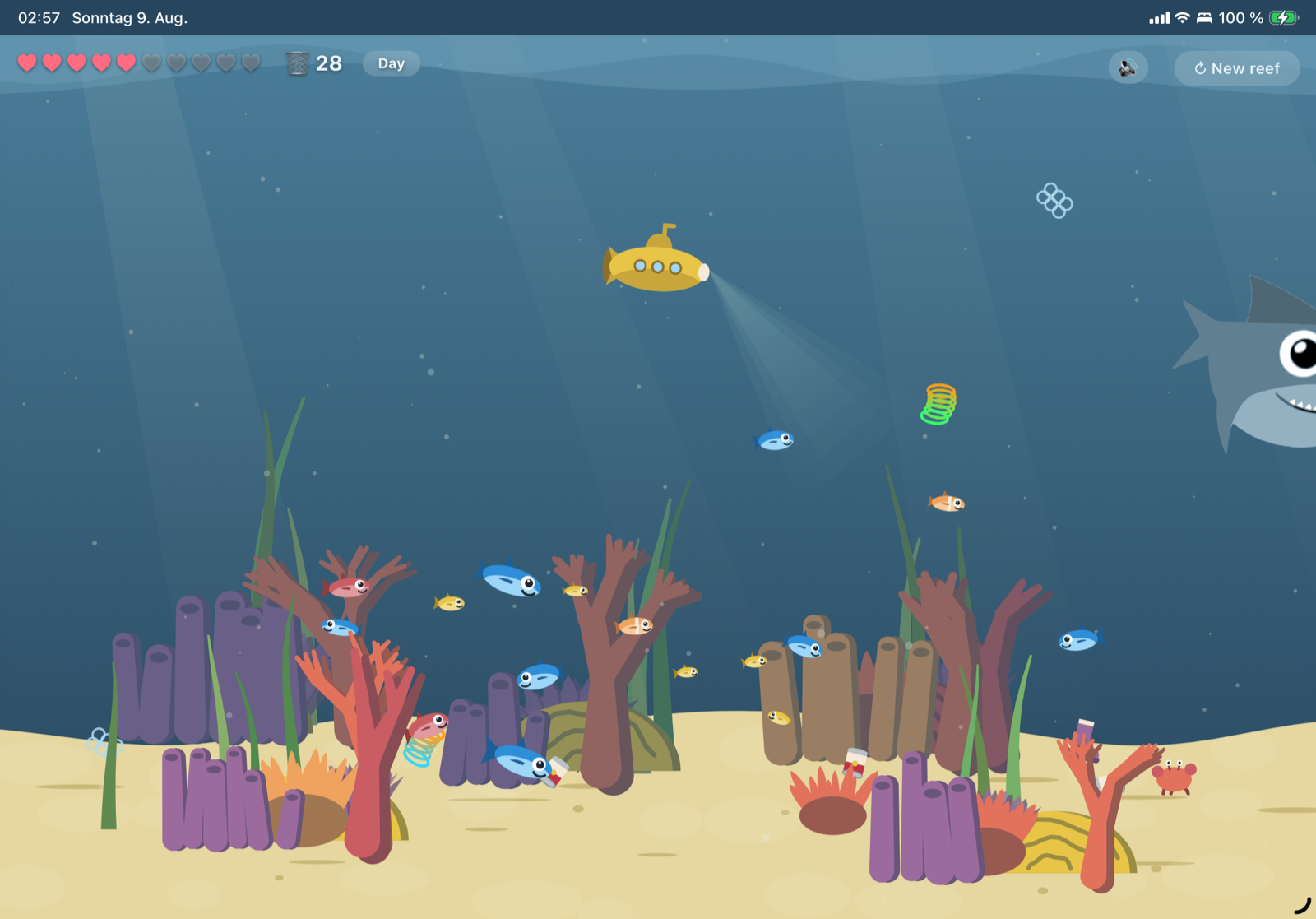 The daylight reef: a yellow submarine with its headlight on, coral and fish across a sandy floor, a slinky and a crab among the litter, and a shark nosing in from the right edge.